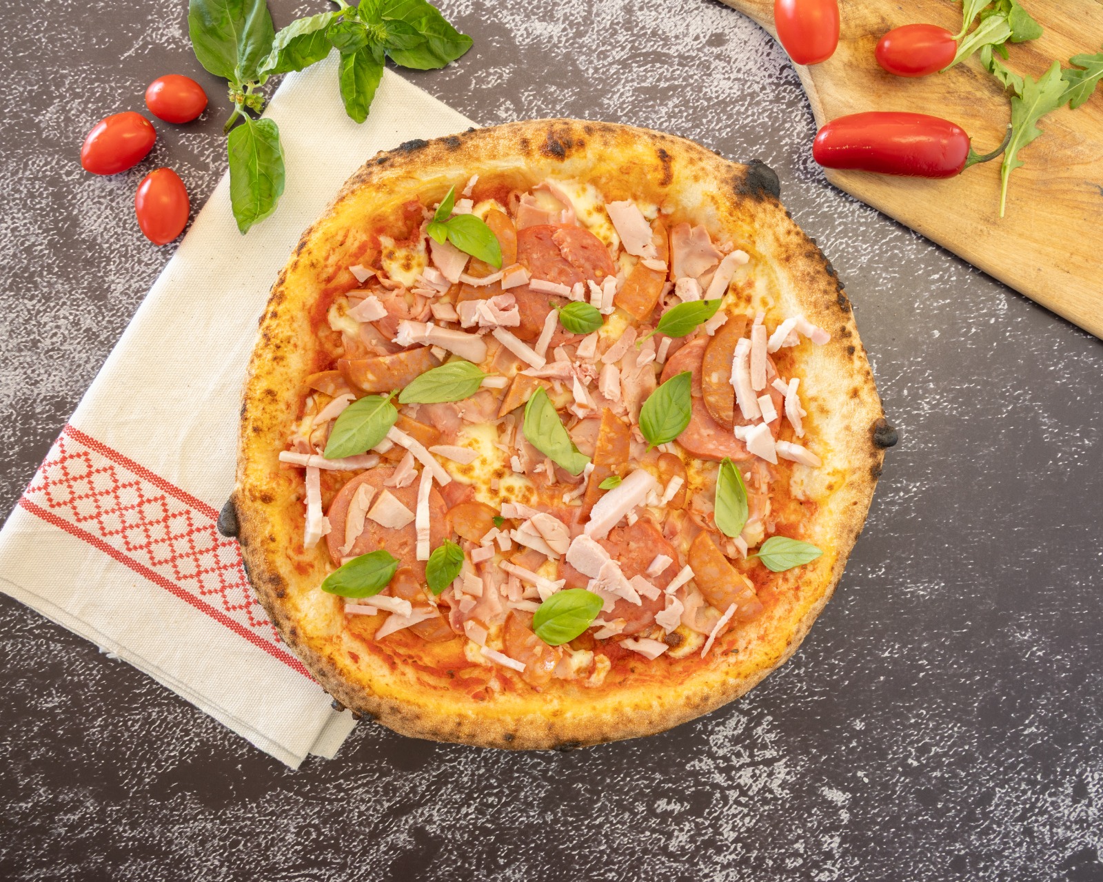 Wood-fired salami and ham pizza topped with fresh basil