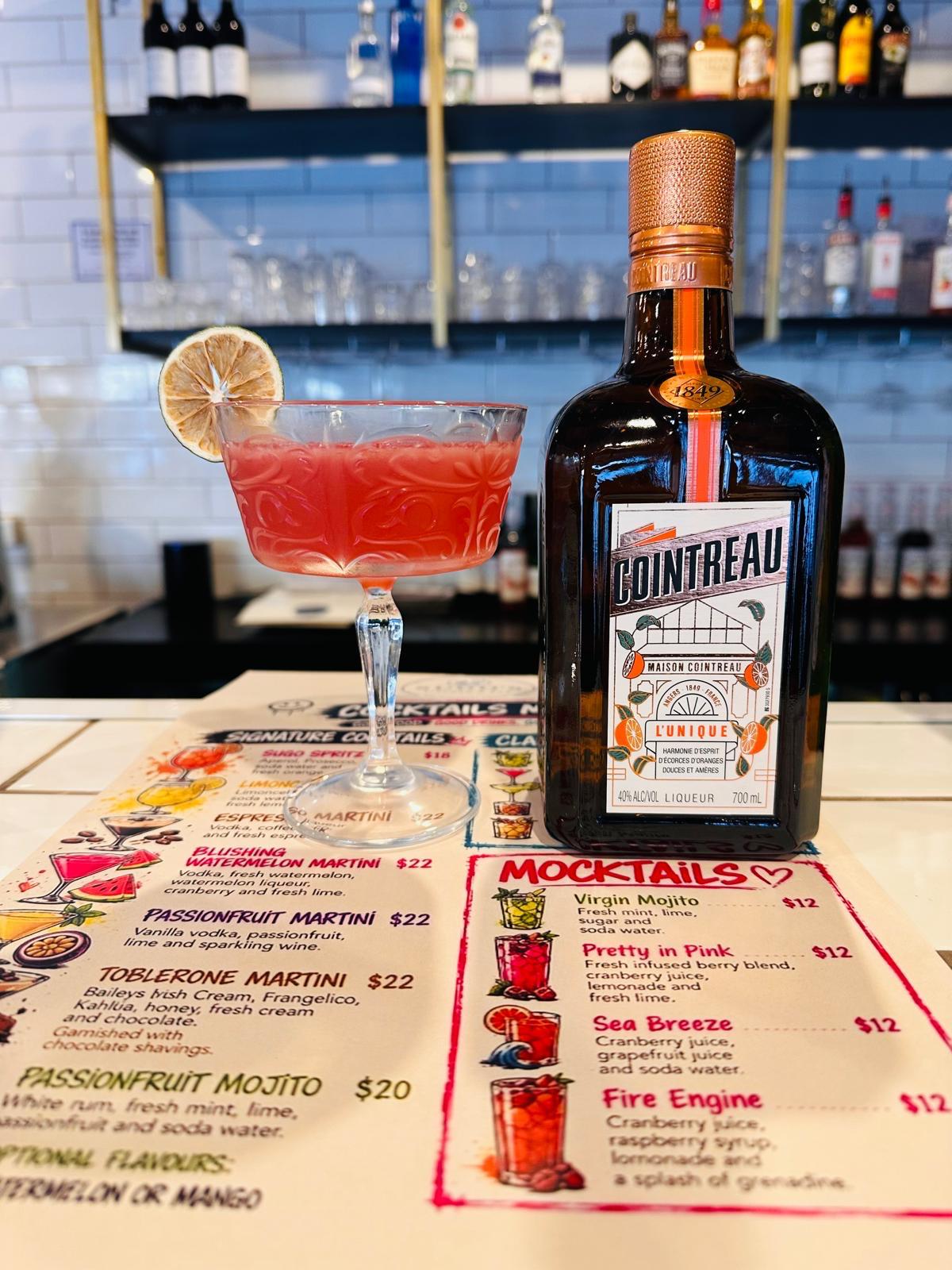Sugo Spritz cocktail beside a Cointreau bottle on the bar